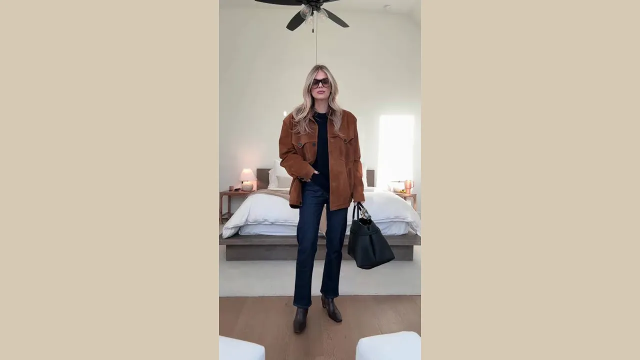 Woman wearing dark blue jeans, a brown jacket, ankle boots, and carrying a black handbag