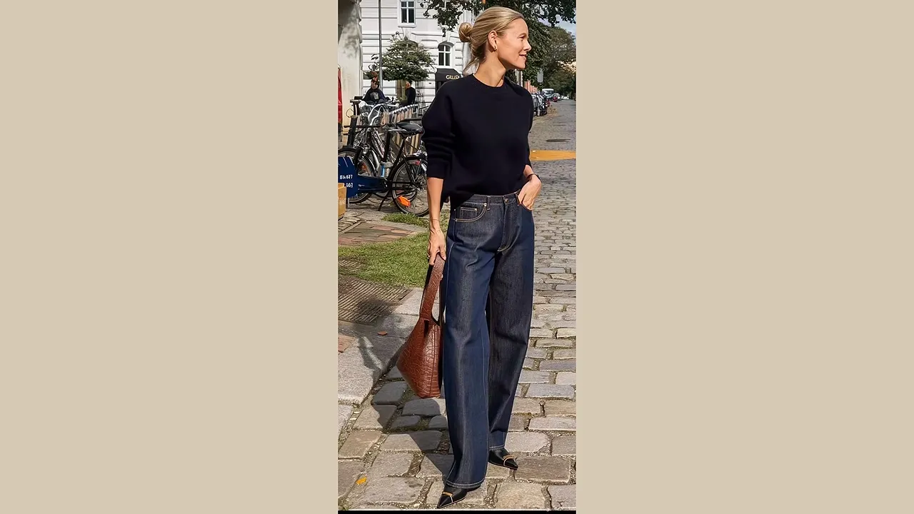 Woman wearing dark wide-leg jeans with a fitted black top and carrying a brown handbag